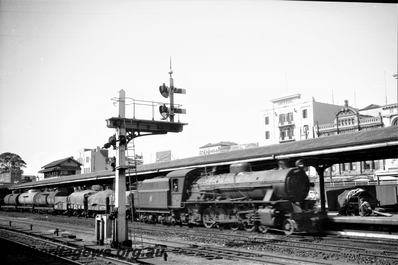 P22439
W class locomotive, on goods train, canopy, platform, bracket signals, city buildings, Perth station, side and front view
