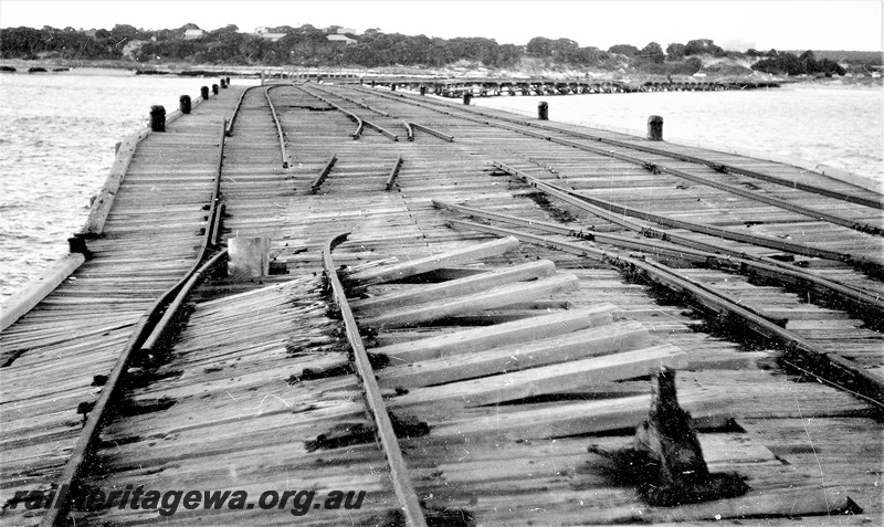 P22467
Storm damage to rails on Hopetoun jetty HR line 1 of 6, showing broken rails and planks, jack, bollards, view towards land from jetty
