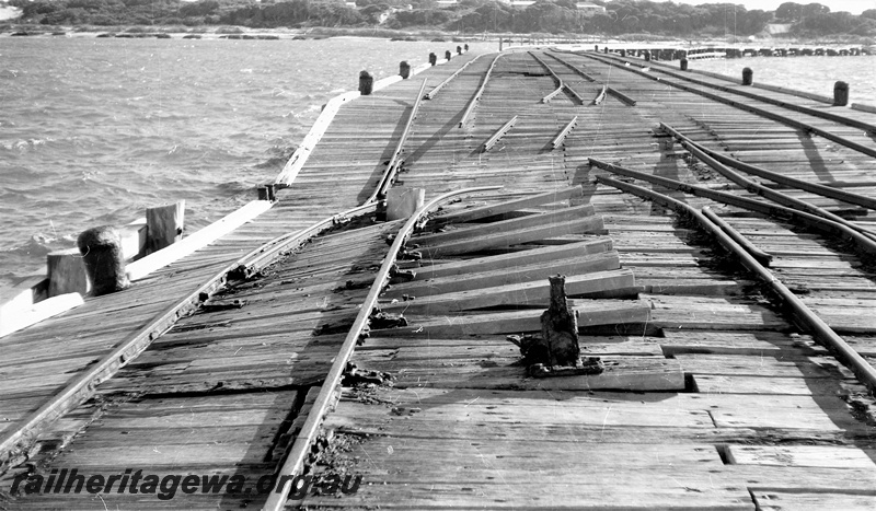 P22470
Storm damage to rails on Hopetoun jetty HR line 4 of 6, disrupted planks, tracks, jack, bollards, view from jetty looking landwards
