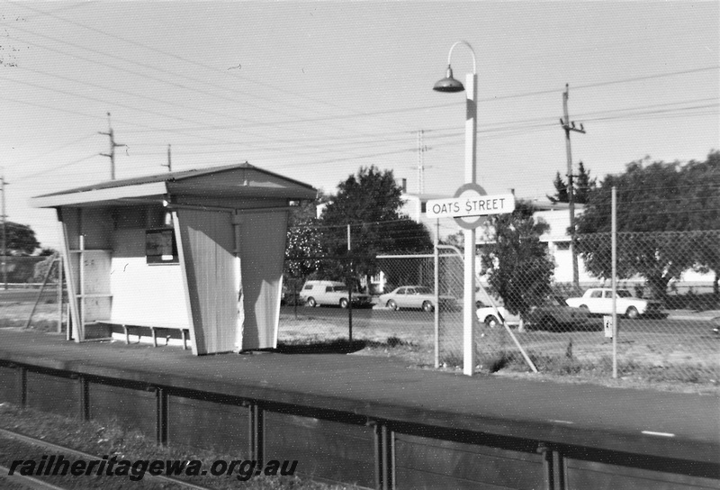 P22474
Oats Street station SWR line 2 of 5, shelter, platform, station sign, light pole, cars on adjacent road, wire fence, view from opposite platform, c1976-1977
