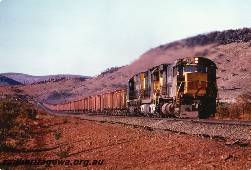 P22570
Hamersley Iron locomotives 4040, 3010 and 4032, triple heading iron ore train, travelling uphill near down end of Swan Loop, Pilbara, side and front view from trackside
