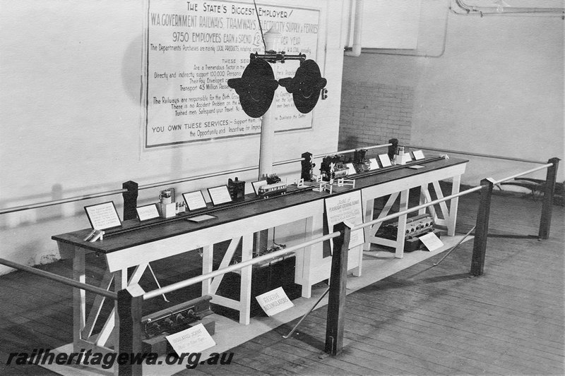 P22577
Display of Western Australian Government Railways items including certificates, light signals, various equipment, model tram running along table top, on display inside building c1940s
