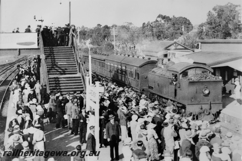 P22583
D class loco on passenger train, station buildings, platforms, name board,  overhead pedestrian footbridge, crowds on platforms and footbridge,  Showgrounds Station, ER line, view from elevated position, c1935

