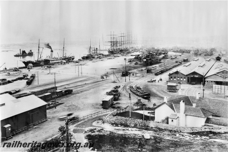 P22585
Overview of Fremantle railway station looking east, old workshop on left, goods shed, Cliff Street crossing in middle of  photo, wharves, steamships and sailing ships in background,. See P02739
