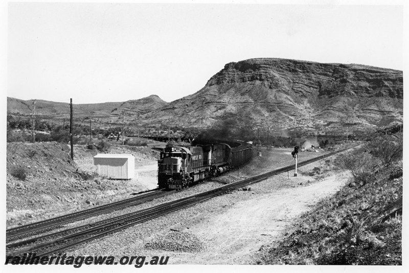 P22591
Hamersley Iron locomotives 4039 and 4036 on rear of up iron ore train comprising 124 wagons, Wombat Junction, Pilbara, trackside shed, colour light signal, rear and side view
