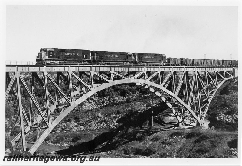 P22592
Hamersley Iron locomotives 3006, 4037 and 3016 triple heading up iron ore train, crossing steel girder bridge, Spring Creek, Pilbara, front and side view
