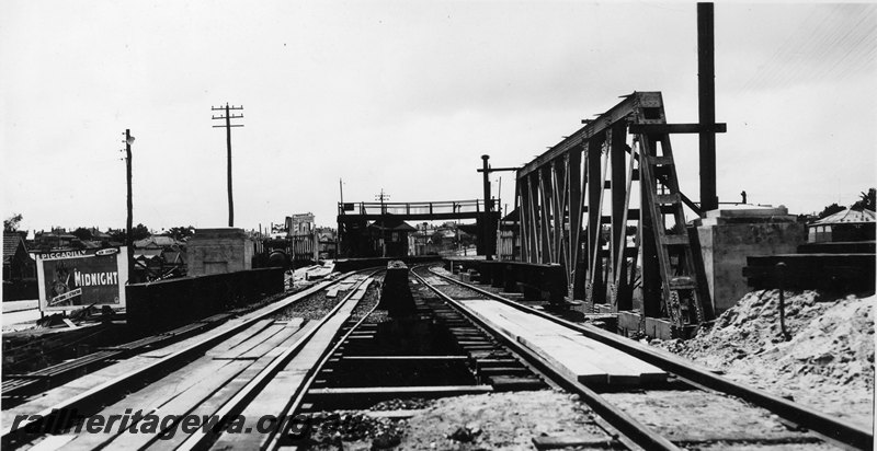 P22757
Extension of Mt Lawley subway ER line No 6 of 15, eastern trusses in place, station building, platform, pedestrian overpass, water crane, advertising hoarding, view along the tracks looking north
