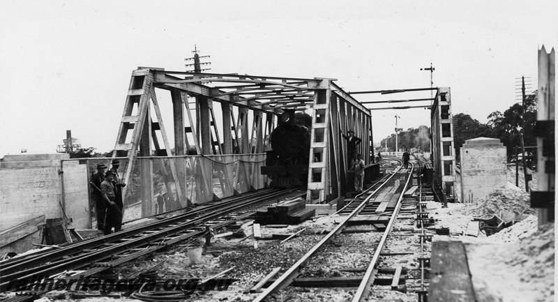 P22761
Extension of Mt Lawley subway ER line No 10 of 15, deflection test, three sets of trusses in place, steam locomotive on bridge, pylons, gasometer, onlookers, view along the tracks looking south
