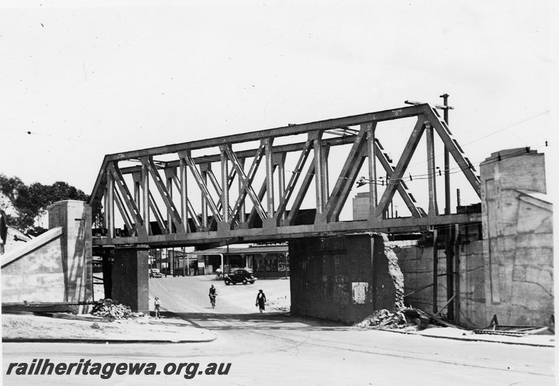 P22762
Extension of Mt Lawley subway ER line No 11 of 15, trusses in place, shops, pedestrians, pylons, partly demolished subway wall, car, view of subway looking west
