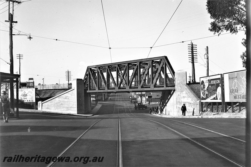 P22765
Extension of Mt Lawley subway ER line No 14 of 15, truss bridge, pylons, pedestrians, advertising hoardings, shop, tram tracks in roadway, tram wires overhead, looking along the roadway towards the east
