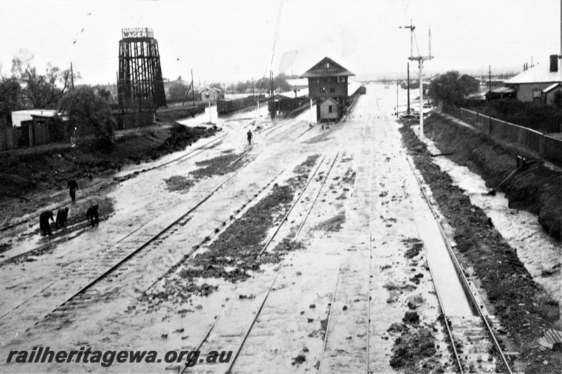 P22797
View of flooded tracks, platforms, canopies, workers, water tower, signal box B, signal, houses, Kalgoorlie, EGR line, view from Maritana Street bridge, c1930
