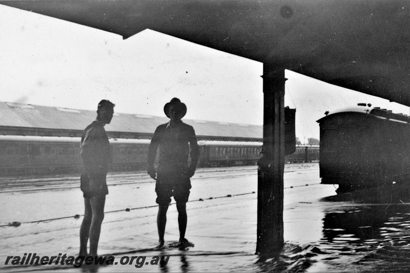 P22798
Flooded station, water level up over platform, canopy, carriages, carriage shed in background, two onlookers, Kalgoorlie, EGR line, view from platform level 
