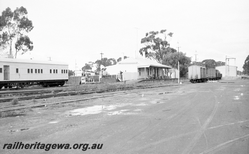 P23958
Station building, platform, yard, loading ramp, goods shed, platform crane, assorted wagons, carpark, Moora, MR line, view from ground level, 
