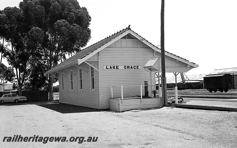 P24261
Station building, weatherboard with tiled roof, platform, van, yard, wheat bin, Lake Grace, WLG line, view from carpark
