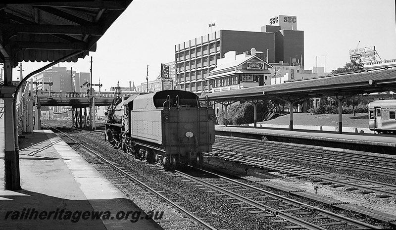 P24267
V class 1215, running light, tracks, canopies, platforms, overhead bridge, city buildings, signals, side and rear view from platform 
