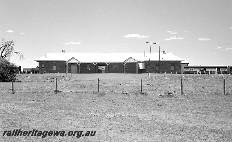 P24287
Station building with metal roof and stone walls, carriages and tanker wagon at platform, Menzies, KL line, view of building from the carpark looking towards tracks 
