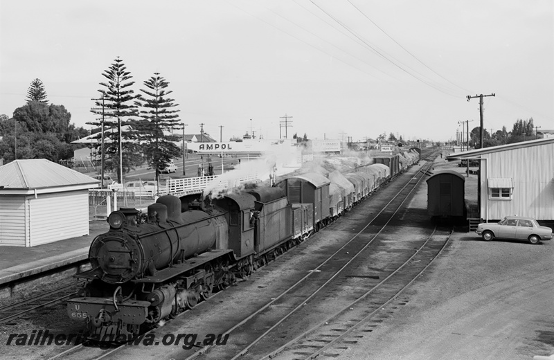 P24372
U class 655 on goods train, platform, station building, goods shed 4th class with van, Ampol garage, Norfolk Island pines, Bassendean, ER line, front and side view from elevated position
