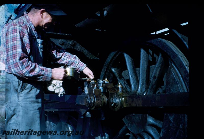 T03326
WAGR driver oiling the motion of his loco dressed in typical attire of bib and braces and a checked shirt
