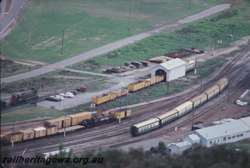 T04320
DA class loco in the green with red stripe livery, rake of six carriages in the foreground, left to right AQL class 290, ARM class and then four AZ class, AL class 414 in the Wagon Repair Depot shed, yellow wagons in the yard, Albany, GSR line, very high elevated view of the yard.
