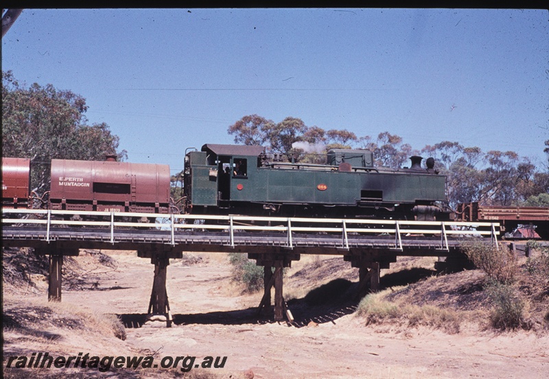 T04442
UT class 664 steam locomotive with 2 JA class water tankers and a HC class low sided wagon crossing a timber bridge over a dry water course. MR line.
