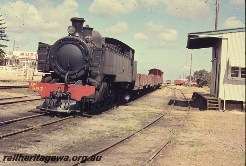 T04565
DD class 597 steam locomotive with a load of empty wagons, goods shed, Bassendean. Ampol service station facing Guildford Road in the background
