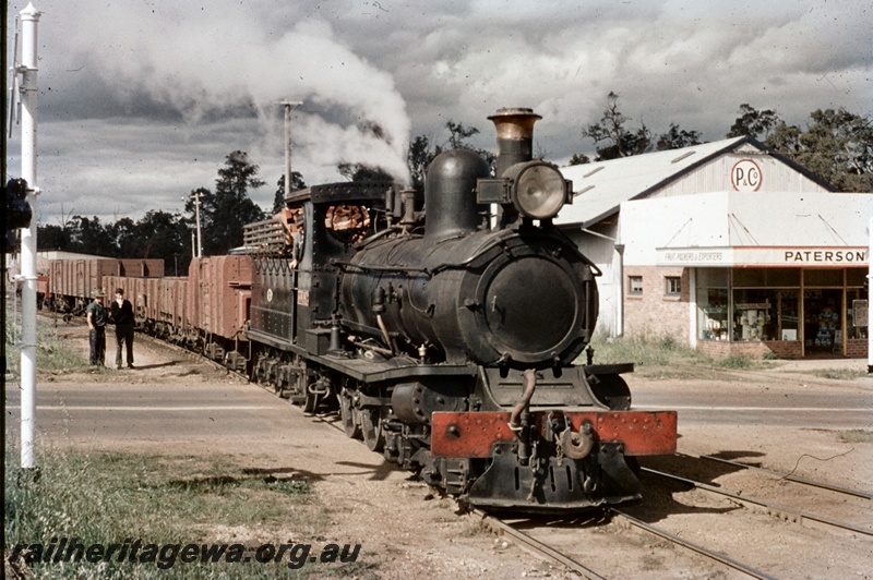 T04700
State Saw Mill SSM No. 2 steam locomotive with a rake of empty wagons, crossing a road, in Manjimup, view along the train.

