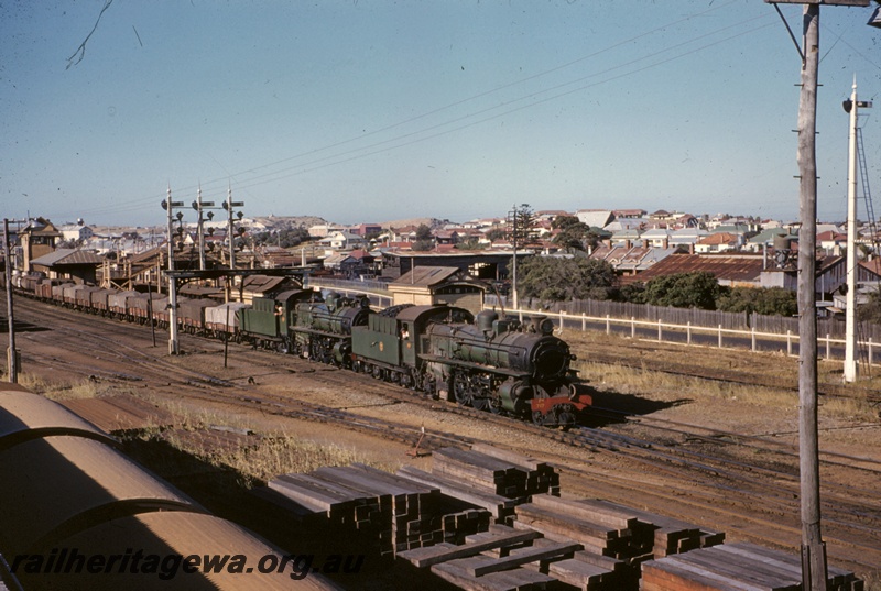 T04878
P M class 717, and another PM type class loco, double heading goods train, signal box, platforms, station buildings, pedestrian overpass, bracket signals, signal gantry, signal, pile of sleepers, North Fremantle, ER line, view from elevated position
