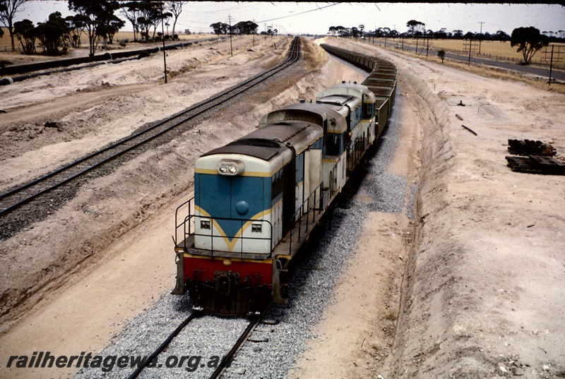 T04885
Two H class locos, double heading ballast train, water pipeline, piles of sleepers, nearing grade crossing between Tammin and Bungulla, EGR line, view from elevated position
