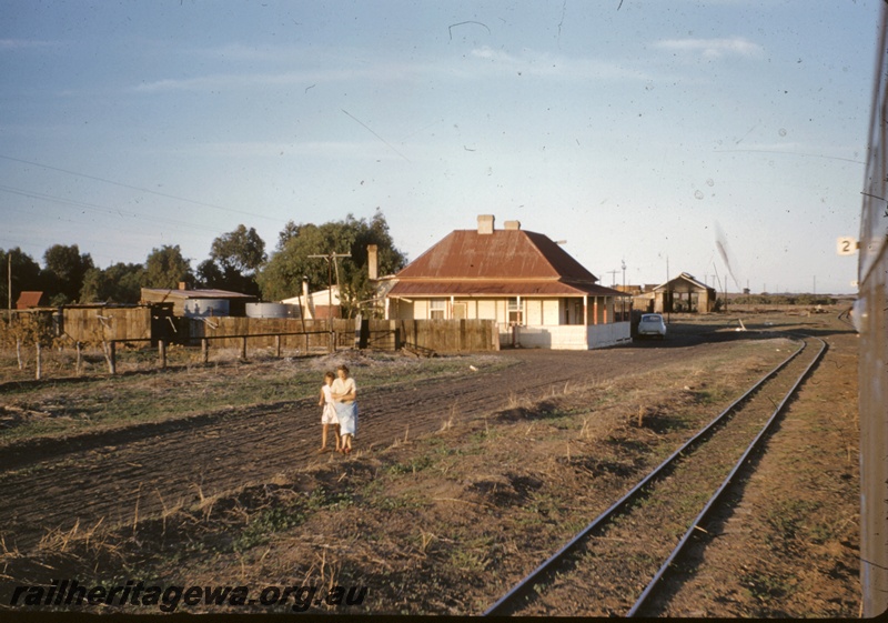 T04939
View of loco depot, shed, sidings, house, car, mother and daughter walking along dirt road near tracks, Walkaway, W line, c1958
