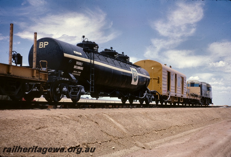 T05021
H class loco hauling steel train including flat car, water tanker BP JTD class 340 (for cooling rails), brakevan, flat wagon with end bulkheads, view from trackside looking towards front of train
