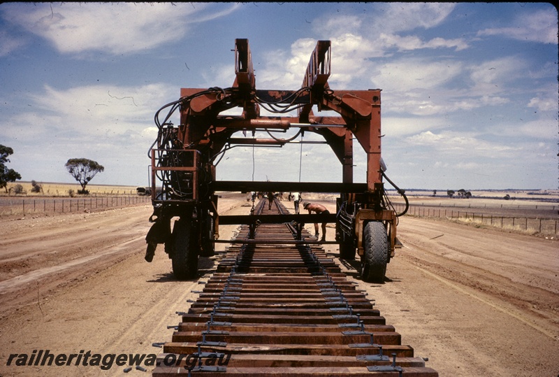 T05026
Track laying, travel lift machine (used to pull rails off flat wagons), sleepers, workers, Hines Hill, EGR line
