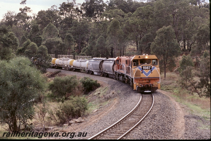 T05278
1 of 2 views of Westrail DB class 1587 in the orange livery with the blue stripe and the loco's number on the front within a black rectangle double heading with another DB class on a Caustic train of JK class tank wagons, view along the train
