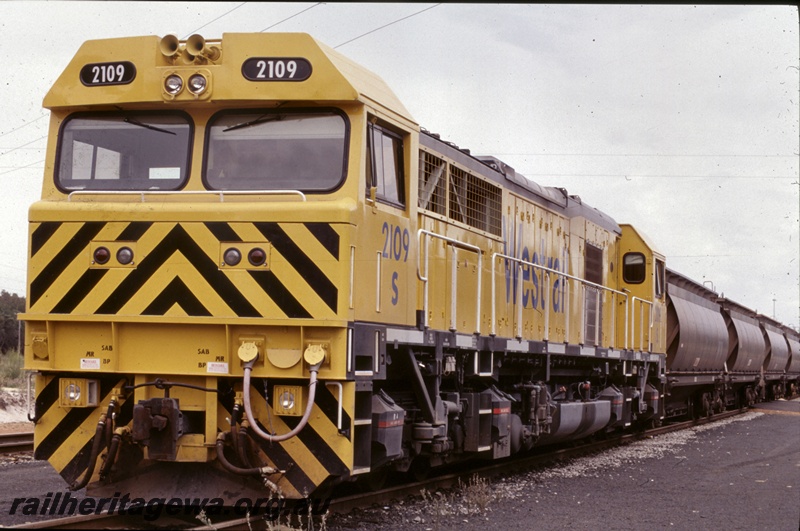 T05282
1 of 2 views of Westrail S class 2109 diesel loco in the yellow livery with black chevrons on the nose hauling an alumina train of XF class wagons at Picton, SWR line, front and side view

