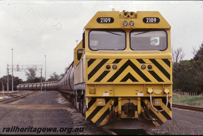 T05283
2 of 2 views of Westrail S class 2109 diesel loco in the yellow livery with black chevrons on the nose hauling an alumina train of XF class wagons, signal gantry, Picton, SWR line, side and front view.
