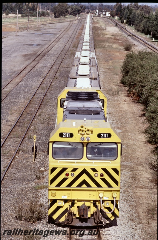T05286
2 of 2 views of Westrail S class 2111 in the yellow livery with black chevrons on the front end hauling an alumina train of XF class wagons at Brunswick Junction, SWR line, front on elevated view of the train
