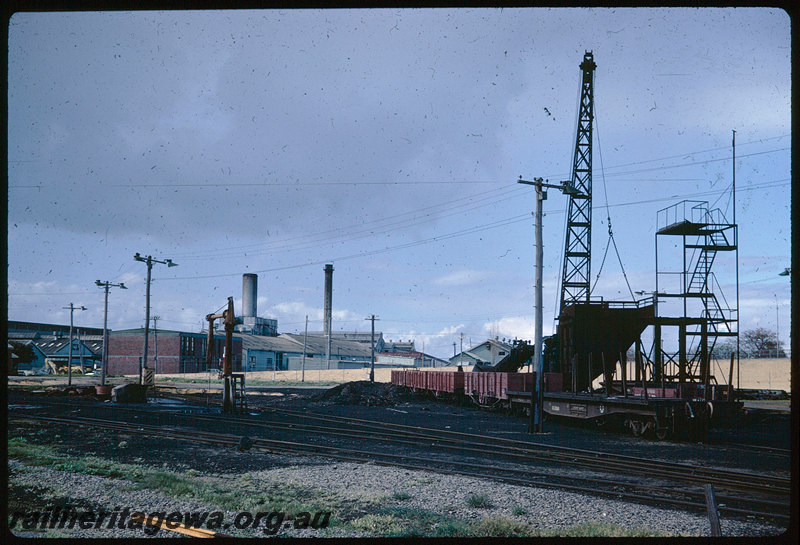 T06221
East Perth Loco Depot, dismantling coal stage at temporary loco depot, QU Class flat wagon, RA Class open wagons, steam crane, water column, approach embankment for East Parade overpass, East Perth Power Station in background
