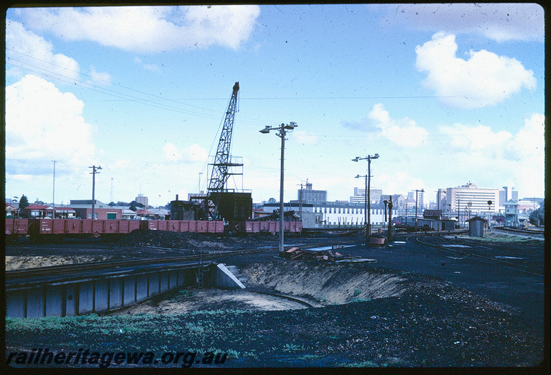 T06222
East Perth Loco Depot, dismantling coal stage at temporary loco depot, QU Class flat wagon, RA Class open wagons, steam crane, water column, turntable, city skyline, Claisebrook station, signal cabin and railcar depot in background
